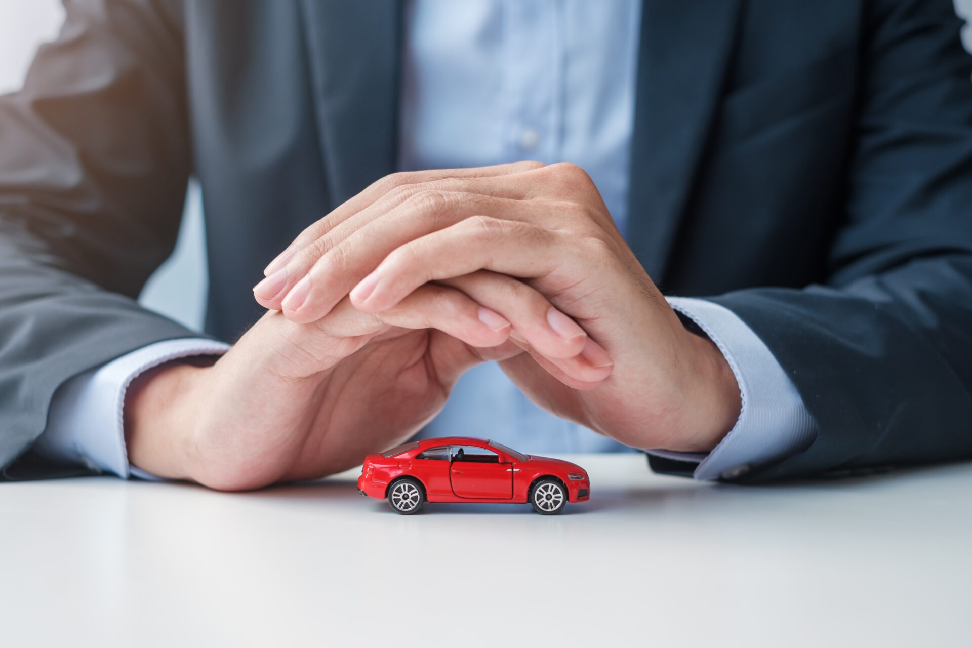 Businessman hand cover or protection red car toy on table. Car i